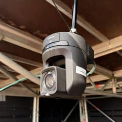 A close-up shot of a black Canon 4K PTZ camera mounted upside down to an overhead metal structure, likely part of a stage or rigging. A "southpoint films" sticker is visible on the side of the camera.