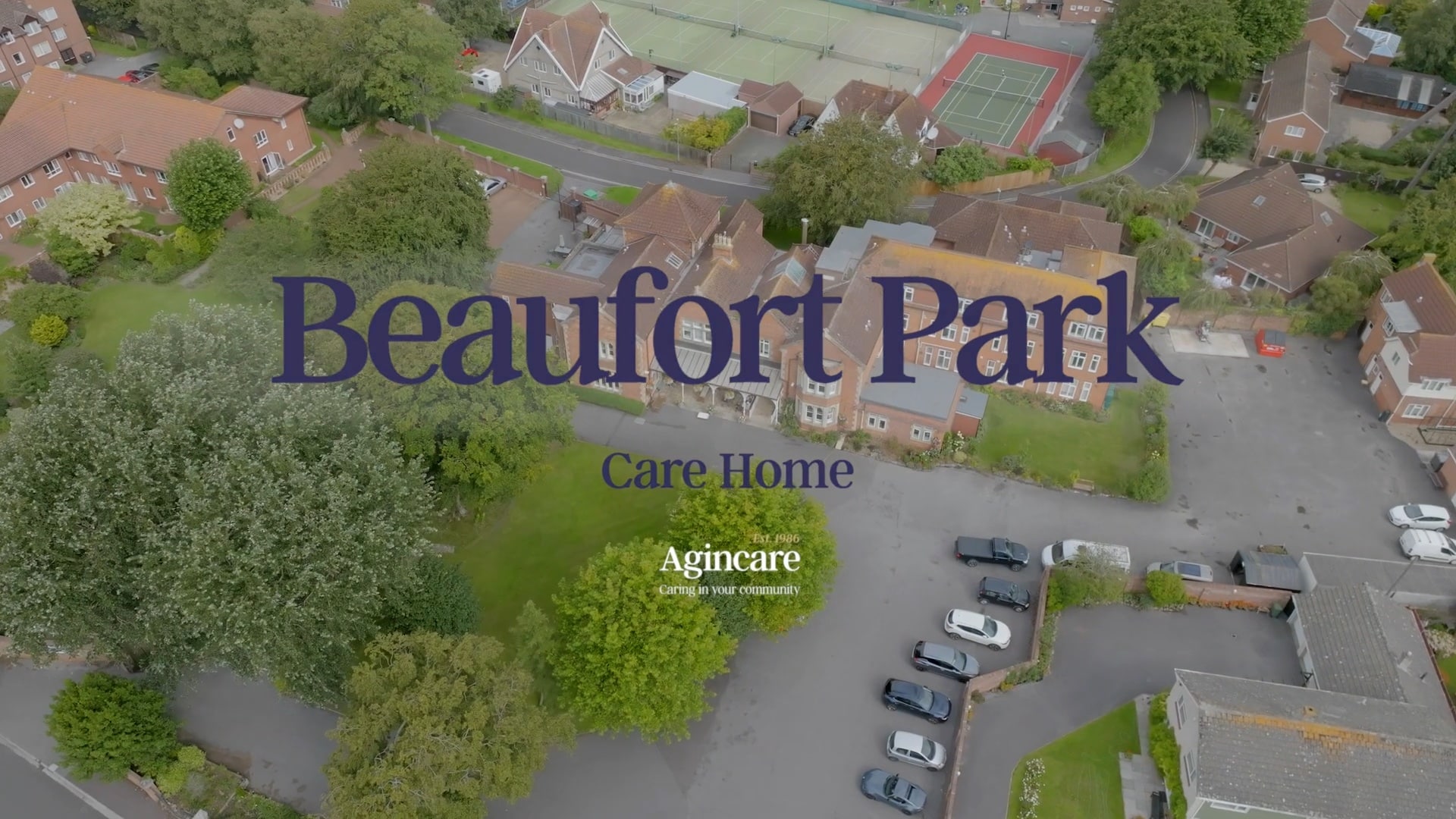 Aerial view of Beaufort Park Care Home surrounded by greenery, residential buildings, and a tennis court. Large text overlay reads "Beaufort Park Care Home" with smaller text "Agincare, Caring in your community" underneath. The image conveys a serene community setting.