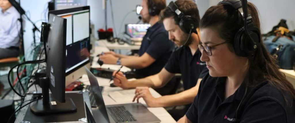 A live video production gallery setup, with people operating video production equipment. The people are wearing headsets to communicate with each other.