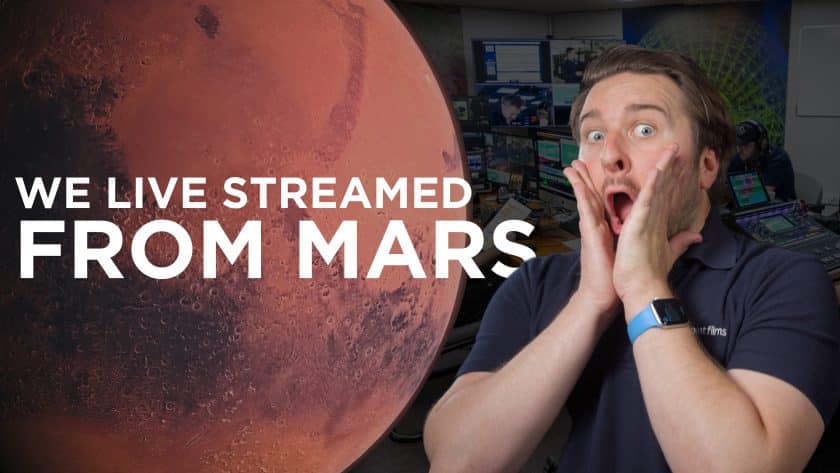 A man with an astonished expression holds his face with both hands in front of a background showing Mars and a control room filled with monitors and technical equipment. Text on the left side of the image reads: "WE LIVE STREAMED FROM MARS." The man is wearing a navy poloshirt and a blue smartwatch band, appearing surprised or excited