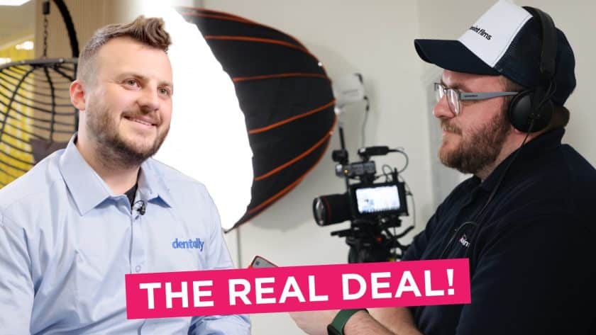 Behind-the-scenes of a video interview: a man in a 'dentally' shirt smiles on camera while a crew member in a 'Southpoint Films' cap and headset monitors the recording. A professional camera and lighting setup is visible, with the caption 'THE REAL DEAL!' in bold pink text across the bottom.