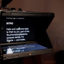 A professional teleprompter displays a script for "Path to Uni," part of the Southampton Sessions podcast series, featuring an intro by Shania. The script is reflected onto a glass pane in front of a camera lens within a production studio setting.