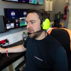 A person wearing a headset with bright yellow ear protection operates a video switcher inside a production trailer.