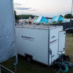 An exterior view of a white "southpoint films" production trailer parked in a field near blue event tents and a crowd.