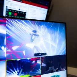 A close-up of a multi-view monitor shows several camera angles of a live concert, including a primary shot of a performer surrounded by dynamic light effects.